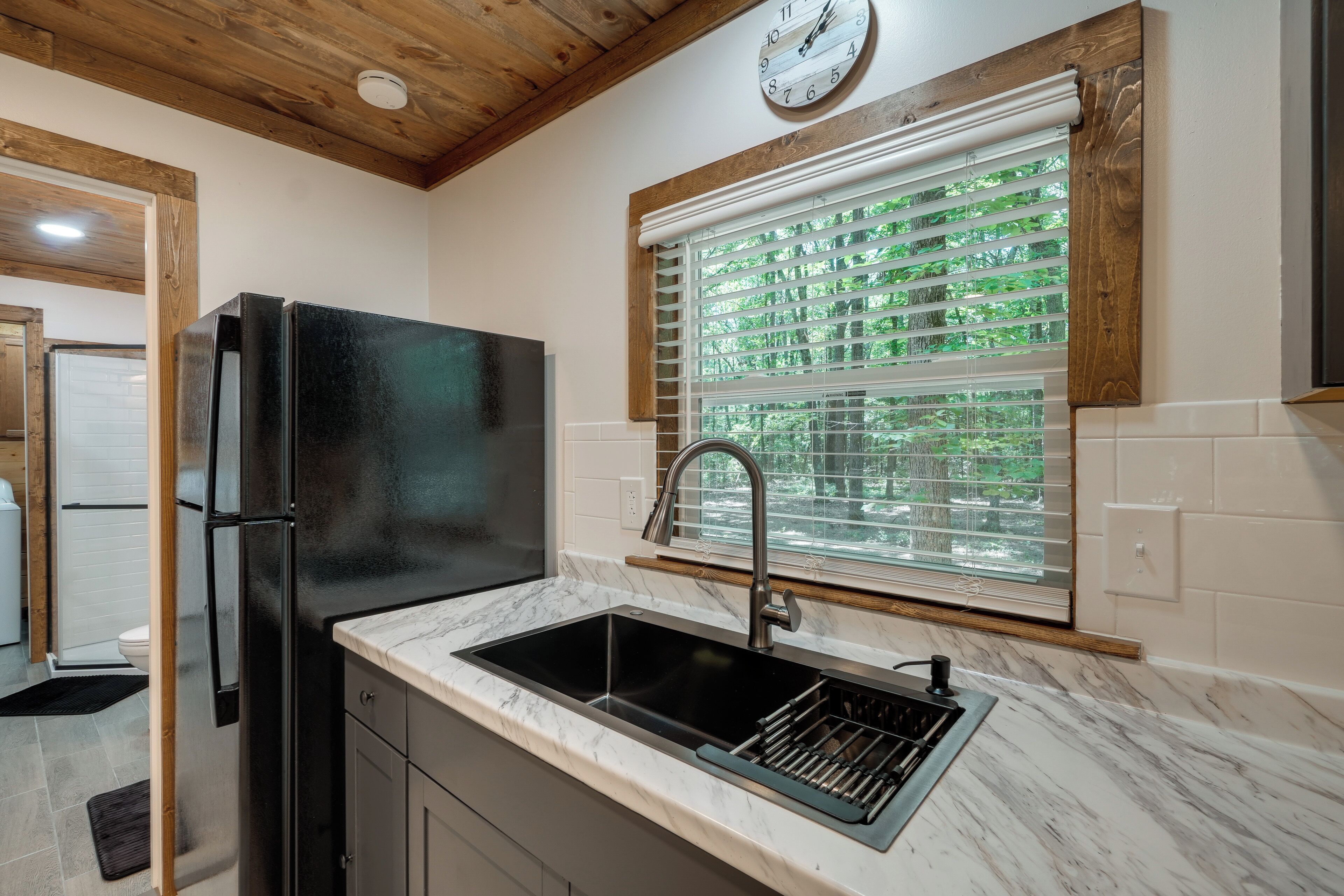A kitchen with a black refrigerator, a sink, and a window with blinds.