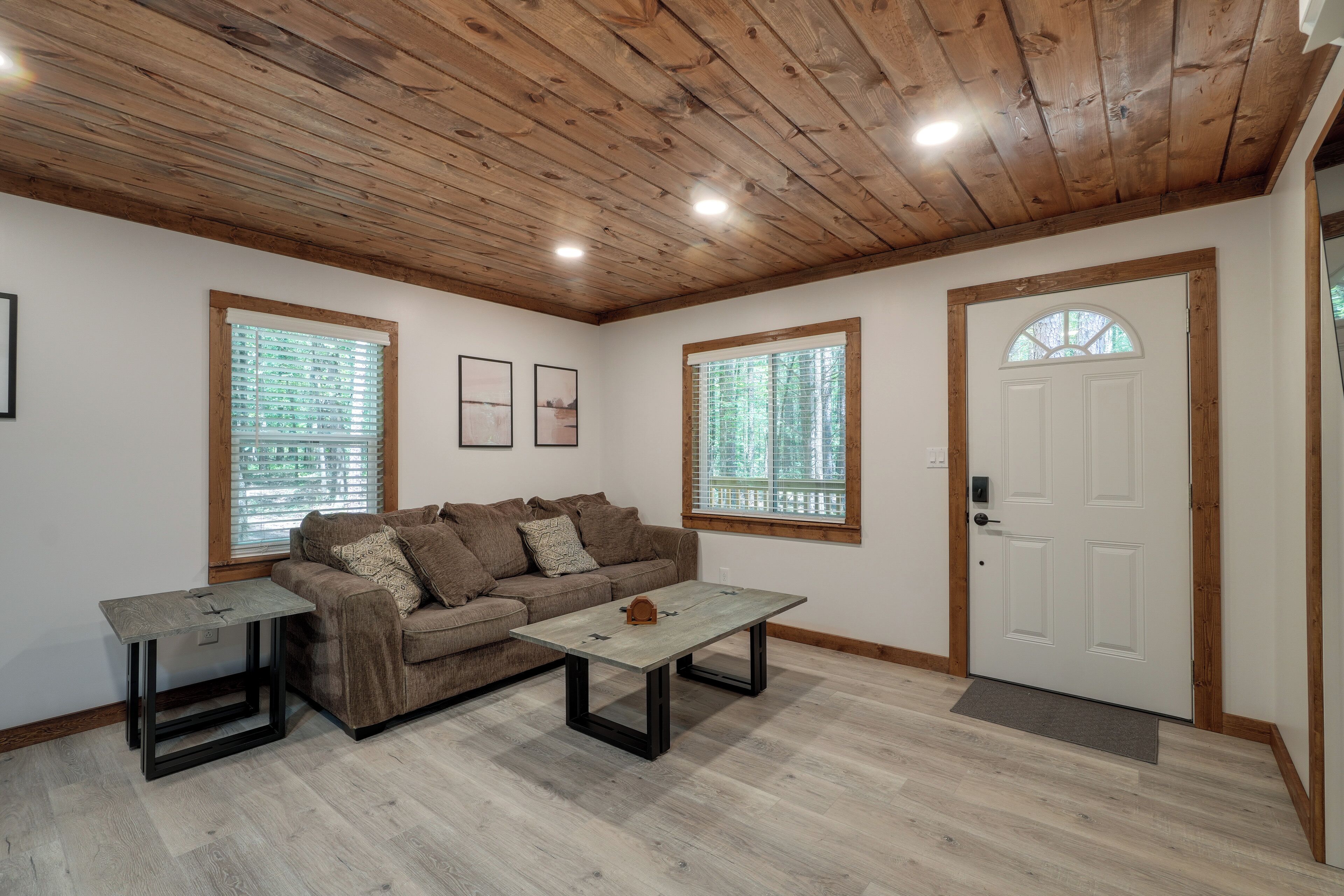 A living room with a wooden ceiling, a brown sofa, two tables, and a white door with a window.