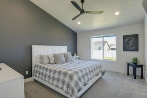 Ein Schlafzimmer mit Bett, Deckenventilator, Fenster und einem kleinen Tisch mit Pflanze.