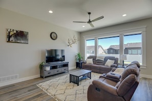 A living room with a flat-screen TV, a ceiling fan, a large window, and a view of houses outside. - 6 Mi to Dtwn! Idaho Falls Escape w/ Private Yard (Idaho Falls)