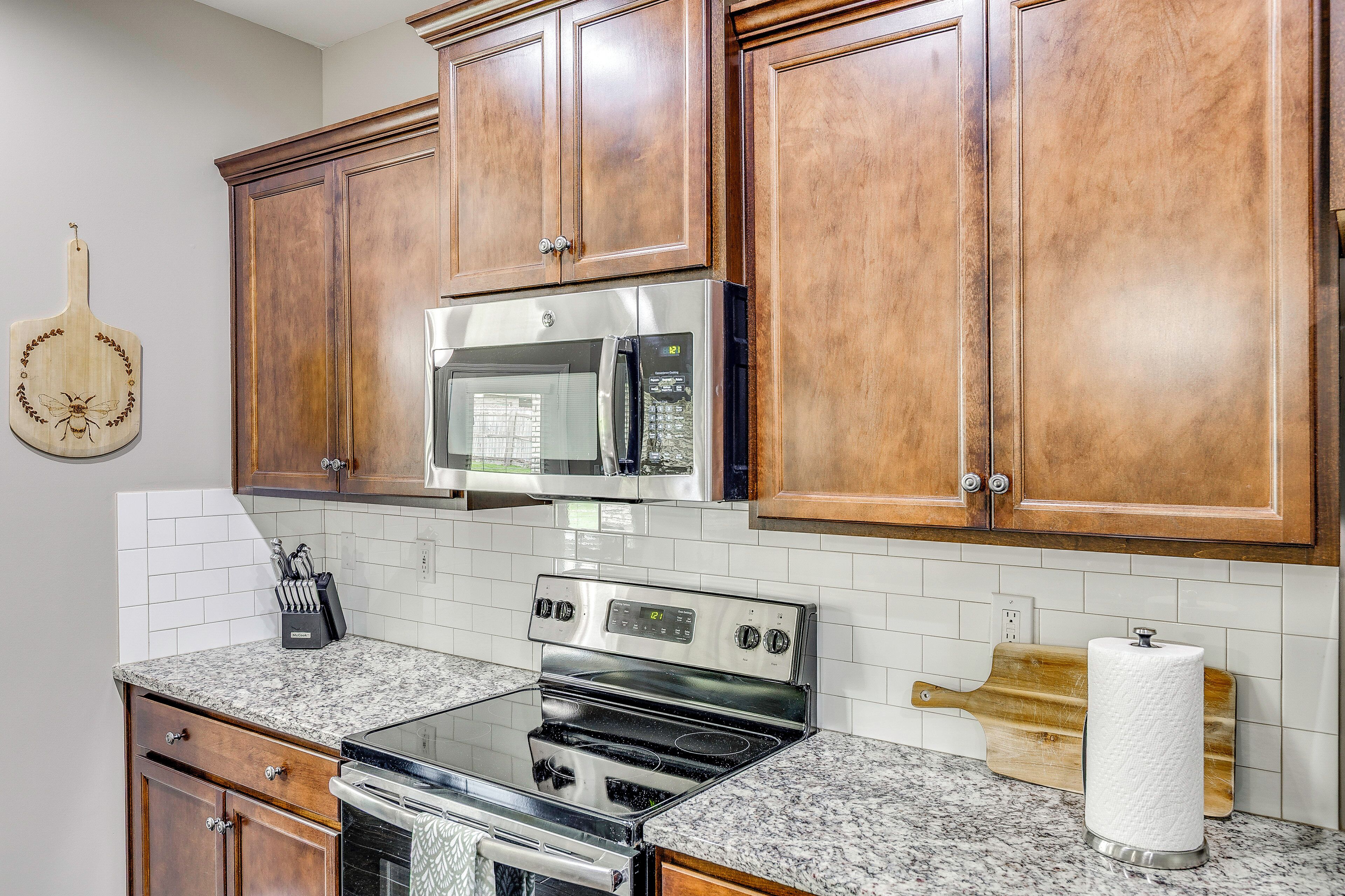 A kitchen with wooden cabinets, stainless steel appliances, a microwave, an oven, a cutting board, and a paper towel holder.