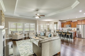 A spacious living room with a sofa, armchairs, and a coffee table. A kitchen with modern appliances and wooden cabinets is visible in the background.