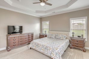 A bedroom with a bed, dresser, television, and a ceiling fan.