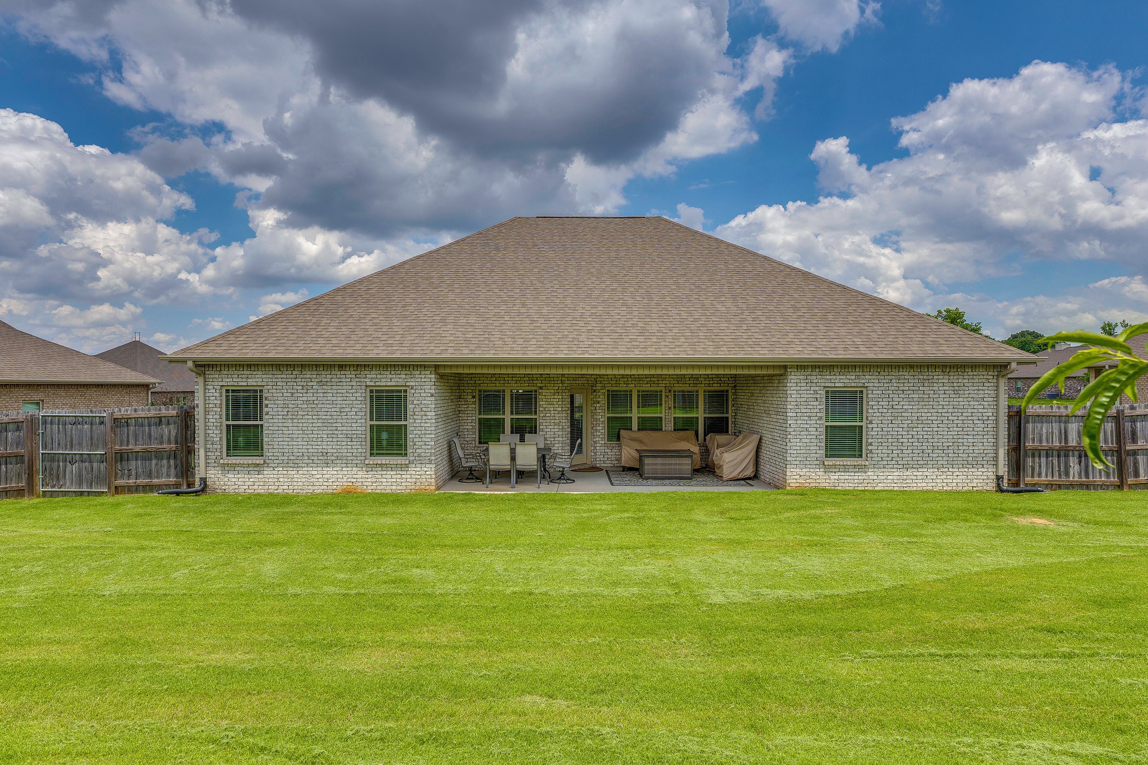 Een gelijkvloers bakstenen huis met een overdekte patio, een gazon en een bewolkte lucht.