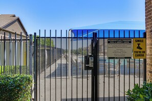 A gated area with a pool and amenity center sign, a 'Smile, You're on Camera' sign, and a blue canopy. - Lewisville Home w/ Pool Access: Walkable Location (Lewisville)