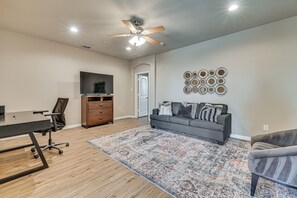 A spacious room with a ceiling fan, a flat-screen TV, a gray sofa, a patterned rug, and a wooden floor. - Lewisville Home w/ Pool Access: Walkable Location (Lewisville)