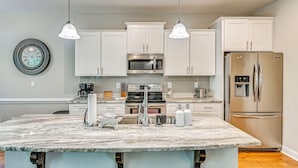 A modern kitchen with white cabinets, a central island, stainless steel appliances, and pendant lighting.