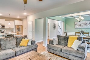 A modern living room with a sofa set, a wooden coffee table, and a dining area with a chandelier. - Stay & Play! Pinehurst Family & Group Golf Retreat (Pinehurst)