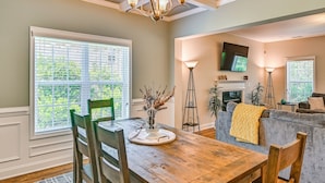 A dining area with a wooden table, chairs, a chandelier, and a window with blinds.