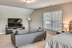 A bedroom with a gray sofa, a TV, a lamp, a bed, and a window with blinds. - Stay & Play! Pinehurst Family & Group Golf Retreat (Pinehurst)