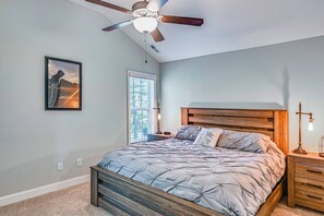 A bedroom with a bed, wooden headboard, ceiling fan, bedside table with lamp, and a window with blinds. - Stay & Play! Pinehurst Family & Group Golf Retreat (Pinehurst)