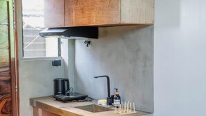 Una cucina compatta con mobili in legno, un frigorifero nero, una macchina da caffè e un lavello.
