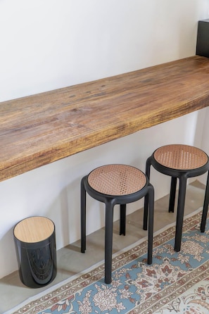 A room with a wooden shelf, two black stools with woven seats, and a decorative rug. - CIELO 2 - steps away from beach, Cloud 9 Siargao (General Luna)