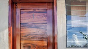 Una porta di legno con il numero '1', un piccolo finestrino che si affaccia sul cielo e sulle nuvole, e un muro in cemento.