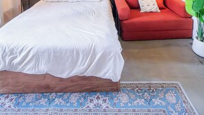 Una camera da letto moderna con un letto grande, un divano rosso, una mensola a parete con una pianta e due lampade a sospensione.