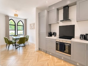 A modern kitchen with grey cabinetry, a black stove, and a dining area with green chairs. - Beautiful House 2BR - Sleeps 6 - Free Parking - Huddersfield (Huddersfield)