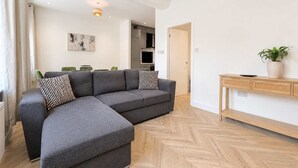 En moderne stue med en grå hjørnesofa, et trækonsolbord og et gulv med et fiskebensmønster.