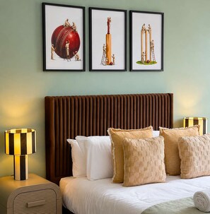 Een hotelkamer met een bed, kussens, een hoofdbord en drie ingelijste kunstwerken aan de muur.