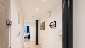 A hallway with a herringbone floor, a black column, and a door on the left. - Stylish 1BR - Sleeps 4 - Free Parking - Manchester (Manchester)