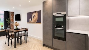 A modern kitchen with a built-in oven, a dining area with a wooden table and chairs, and a large abstract painting on the wall. - Stylish 1BR - Sleeps 4 - Free Parking - Manchester (Manchester)