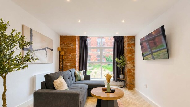 A modern living room with a sectional sofa, a round coffee table, a potted plant, and a large window with a view. - Stylish 1BR - Sleeps 4 - Free Parking - Manchester (Manchester)