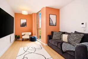Een woonkamer met een donkere bank, een witte fauteuil, een zwart-wit kleed en twee ingelijste foto’s aan de muur.