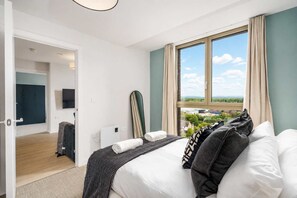 A hotel room with a bed, a TV, a window with curtains, and a view of the outside. - Luxury Views 10th Floor 2 Bed Apartment (Manchester)