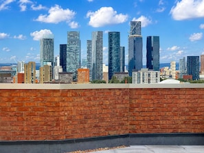 A city skyline with modern skyscrapers, a brick wall in the foreground, and a clear blue sky. - Stylish 1 Bed Sleeps 3 - Old Trafford - City Centre Tram Access (Manchester)