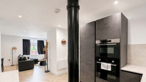 Et moderne køkken med indbygget ovn og spiseområde med sofa og gulvlampe.