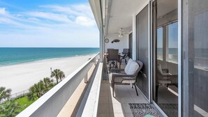 Een balkon met uitzicht op het strand, een plafondventilator en een stoel.