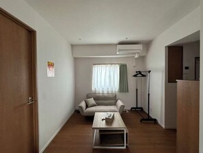Ein schlichter Wohnraum mit einer Couch, einem Couchtisch und einem Fenster mit Vorhängen.