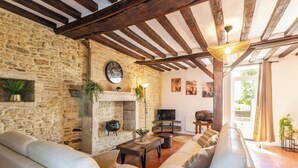 Un salon aux murs en pierre, doté d’une cheminée, de canapés en cuir, d’un téléviseur et d’un plafond en bois.