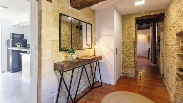 Un couloir aux murs de pierre, agrémenté d’une console en bois rustique, d’un miroir et d’une plante en pot.