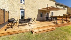 Un bâtiment en pierre doté d’une terrasse en bois, d’un espace extérieur aménagé pour s’asseoir et d’un barbecue.