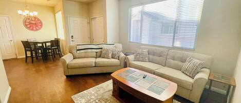A living room with a sofa, coffee table, and dining area with chairs and a clock.
