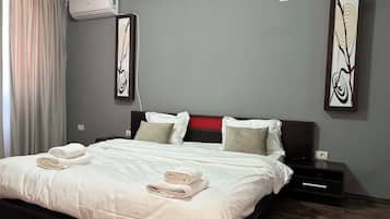 Un lit bien fait, avec du linge de lit et des serviettes blancs, une tête de lit sombre et deux œuvres d’art accrochées au mur.