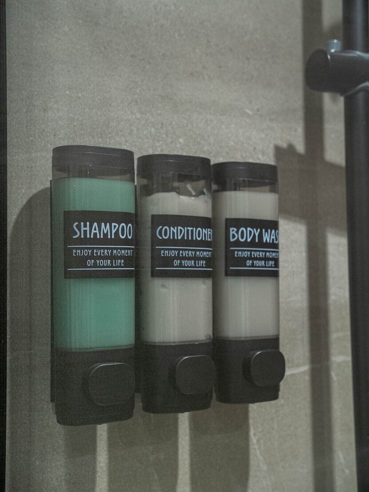 Trois distributeurs de produits de toilette étiquetés « Shampoing », « Après-shampoing  » et « Gel douche », et portant des messages inspirants.