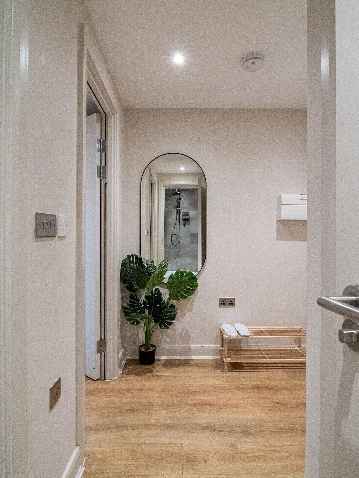 Un couloir avec un plancher en bois, une plante en pot, un miroir et un espace douche.