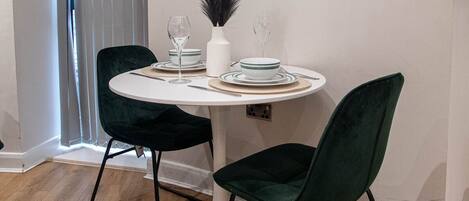 A dining area with a round table, two dark green chairs, white plates, and a vase with feathers.