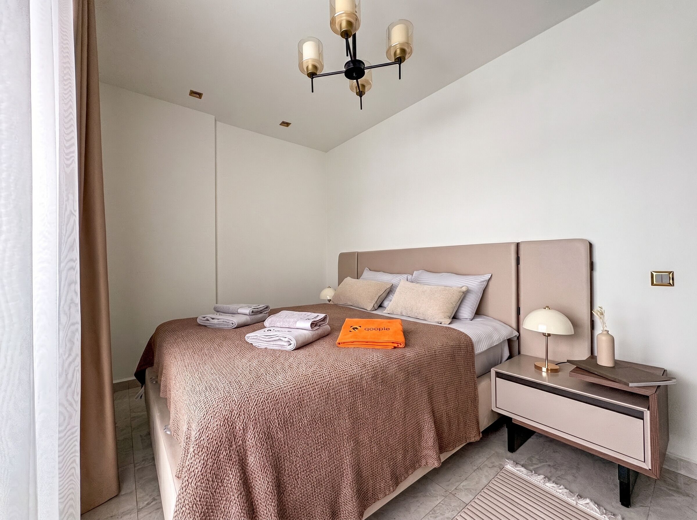 A neatly arranged bedroom with a bed, bedside table, lamp, and a hanging light fixture.
