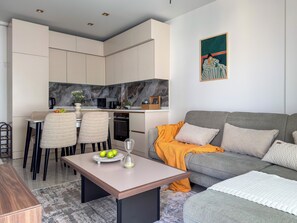 Un salon moderne avec un canapé gris, une table basse et un coin repas comprenant des chaises, et une cuisine en arrière-plan.