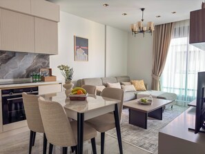 Una sala de estar moderna con comedor, un conjunto de sofás, un televisor y una cocina con salpicadero de mármol.