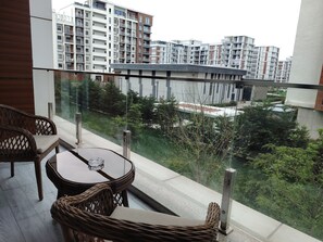 A balcony with wicker furniture, a glass railing, and a view of high-rise buildings and greenery. - 2-bedroom apartment with balcony in tranquil Ташкент with AC for relaxing stays (Ташкент)