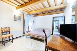 A bedroom with a bed, a chair, a television, and a wooden ceiling.