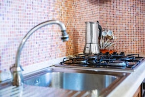 A kitchen with a gas stove, a sink, and a kettle.