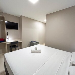 A hotel room with a bed, a desk, a chair, a TV mounted on the wall, and a small table with a towel on it. - Riviera Hotel Brasilia (Brasília)