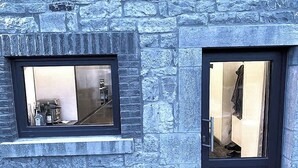 Un edificio de piedra con dos ventanas; una muestra una zona de cocina y la otra, una habitación con una puerta.