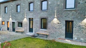 Un edificio de piedra con varias ventanas y puertas, un patio empedrado y mesas al aire libre.