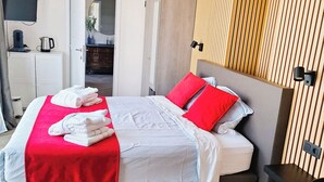 Habitación de hotel con una cama, colcha roja y blanca, pared de paneles de madera, televisor y una mesita de noche con lámpara.