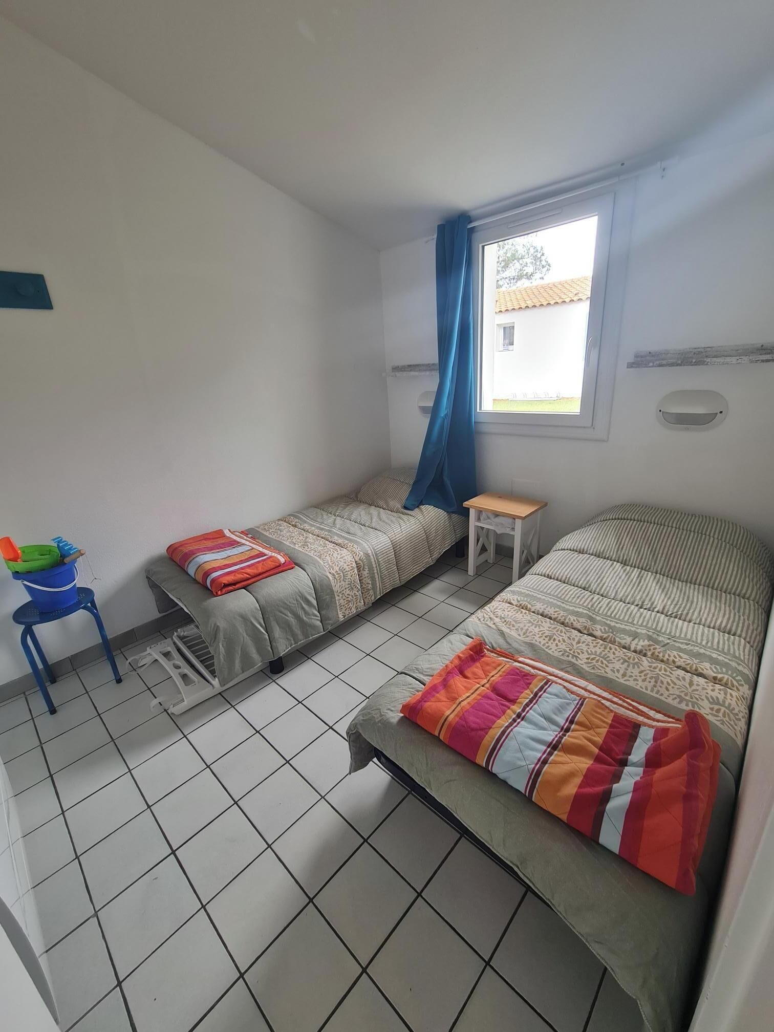 Una camera del dormitorio con due letti, un tavolino, una sedia e una finestra con tende.